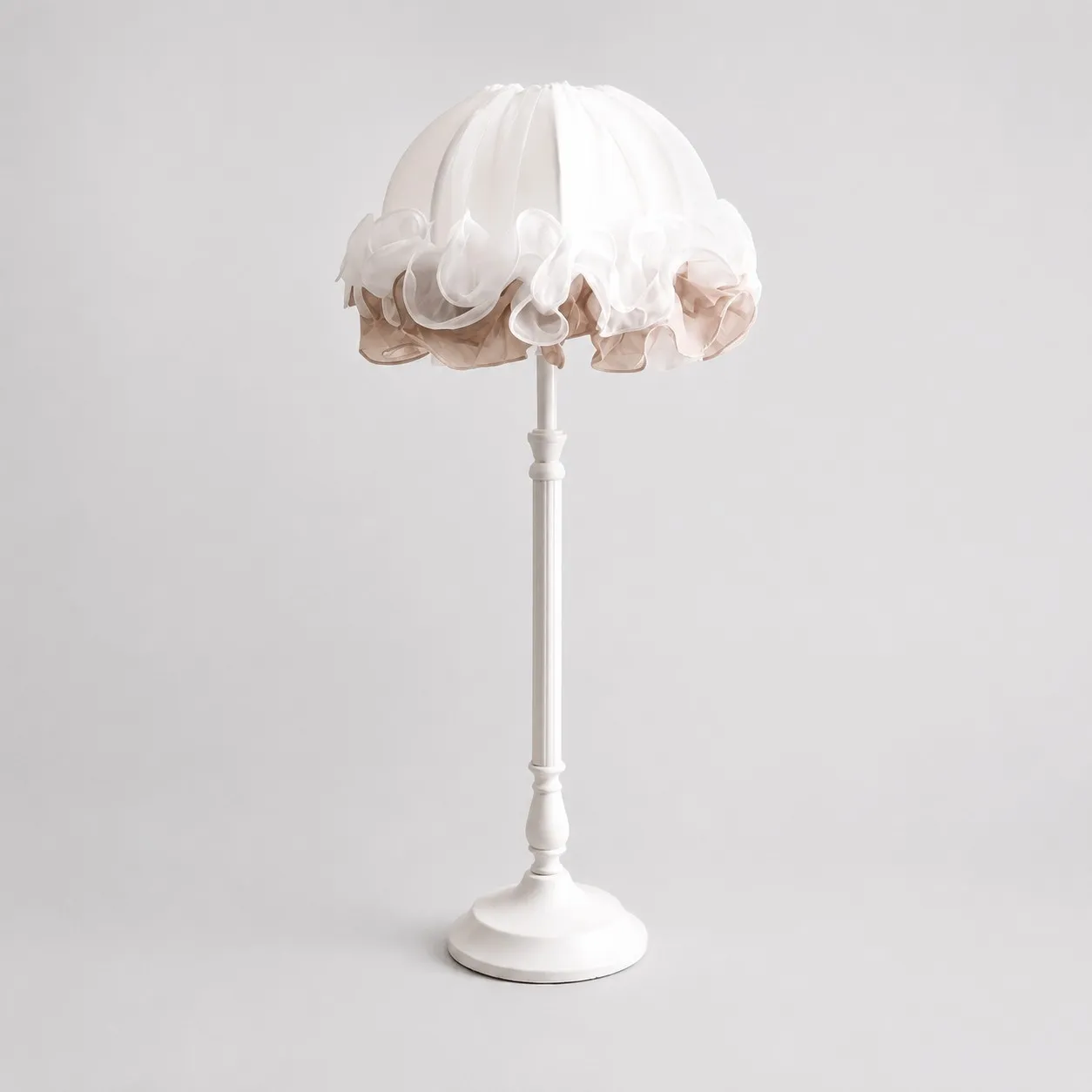 Front view of pure white ruffled fabric table lamp with sculpted metal stem