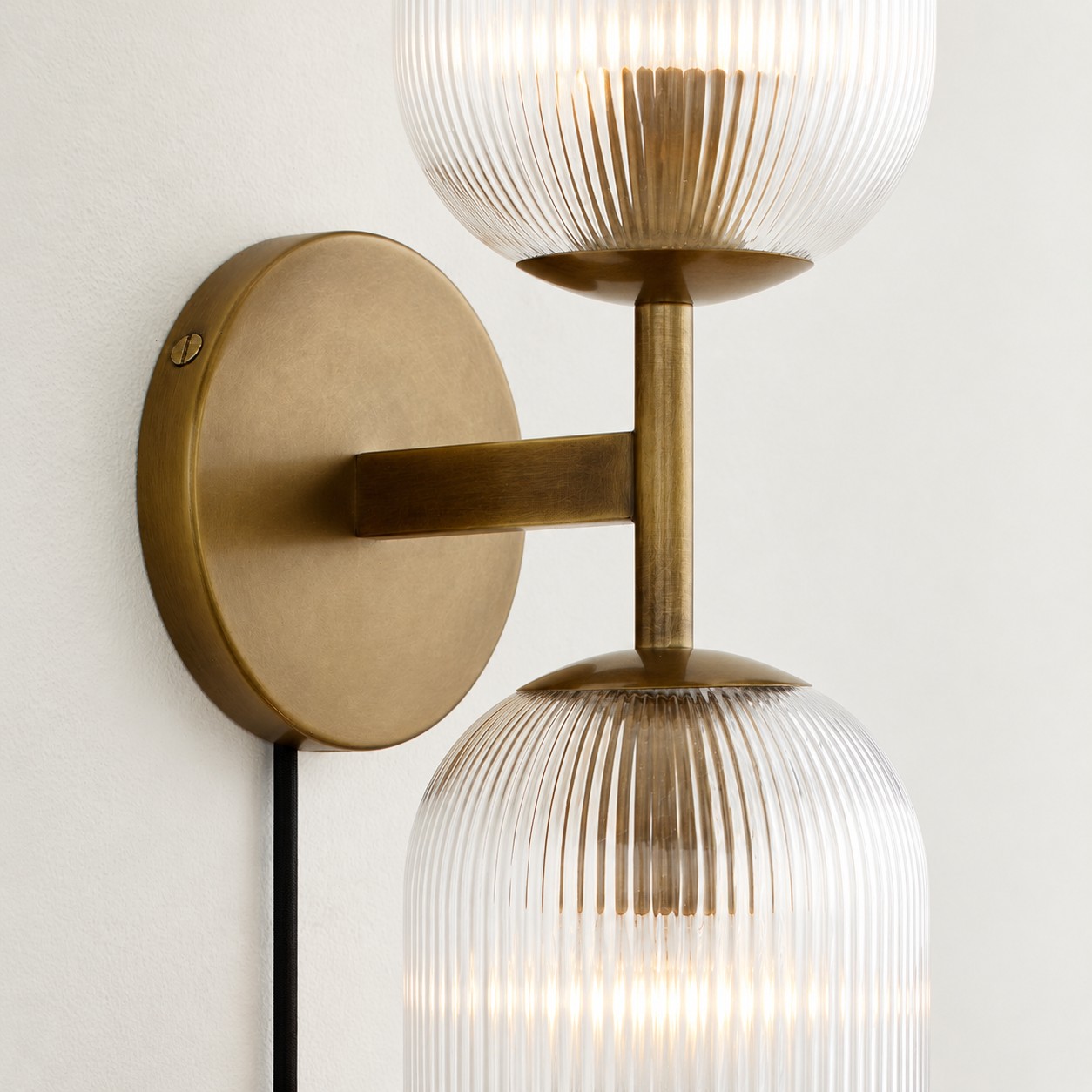 Close view of two tumbled-brass ribbed shades and the shared arm